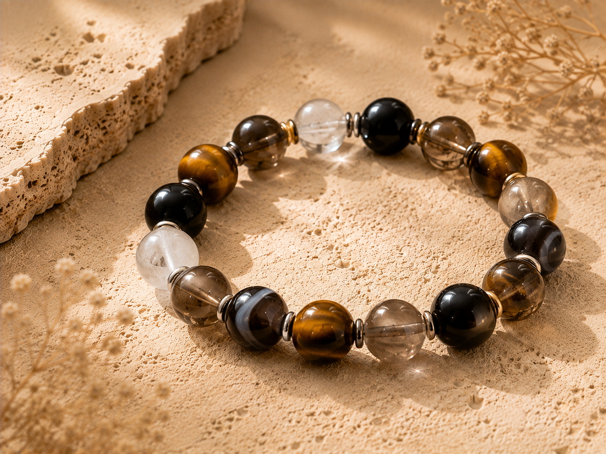 Protective crystal beads including black obsidian, smoky quartz, tiger eye, clear quartz, and agate on a warm stone surface